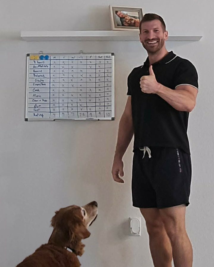 Chandler giving a thumbs up next to his habit whiteboard, with his dog Max looking on